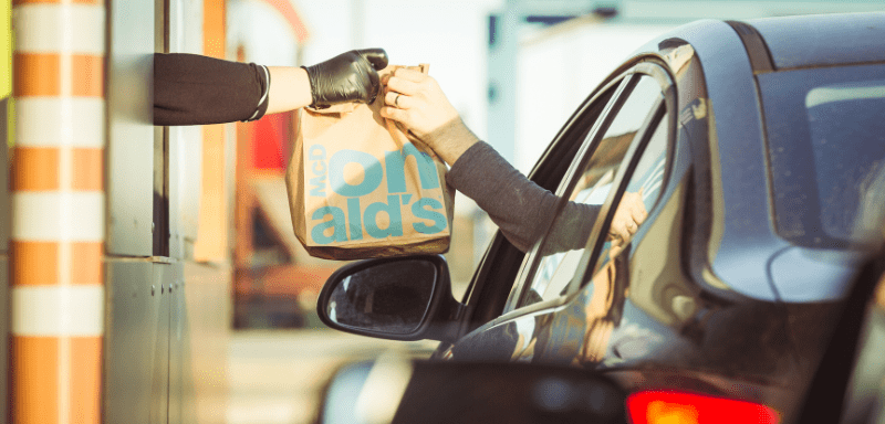 Drive thru do McDonal's, onde trabalhador entrega pacote de comida para passageiro no Carro, representando trabalho no McDonald's.