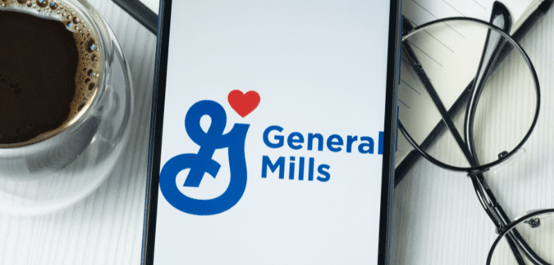 Logo da General Mills em celular ao lado de óculos e café.