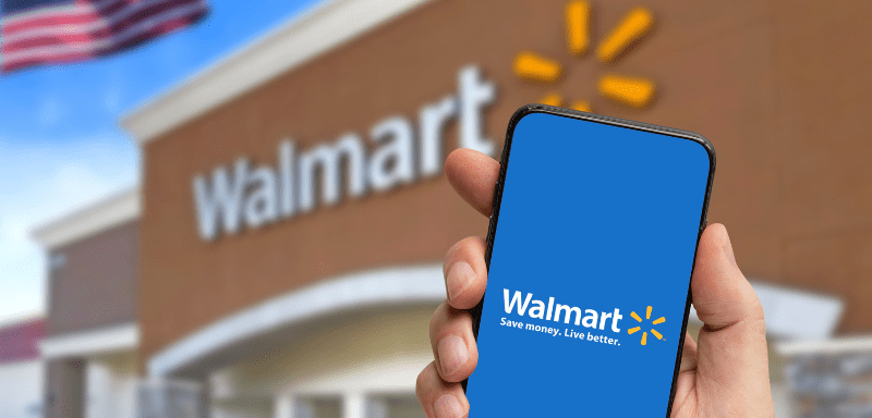 Logo do Walmart em celular, em frente a estabelecimento da empresa.